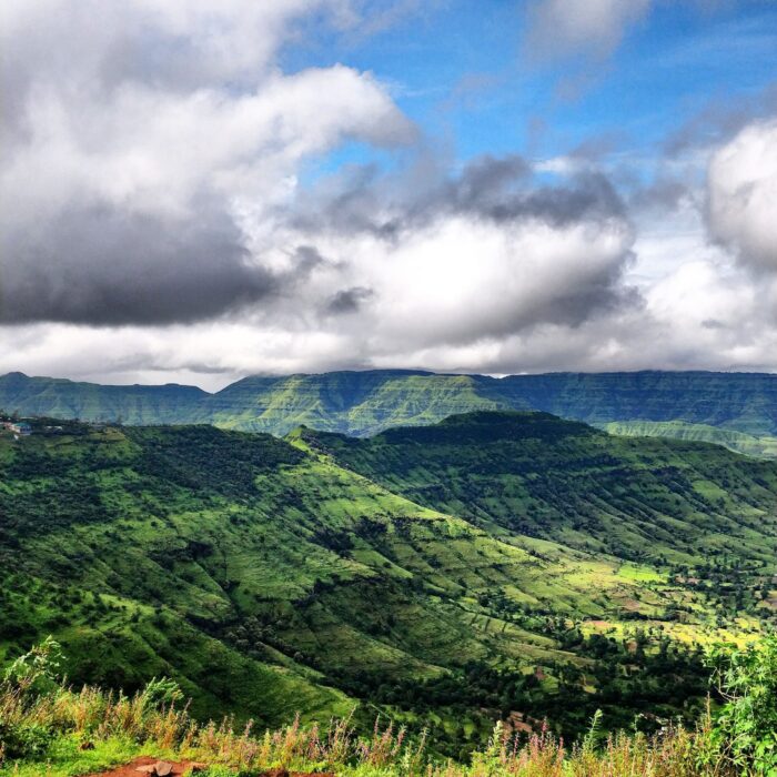 Vast green valley with terraced hills under a cloudy sky and distant mountains on the horizon.